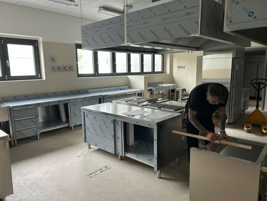 Zona preparazione alimenti con tavoli armadiati inox, lavelli professionali e postazioni operative ergonomiche